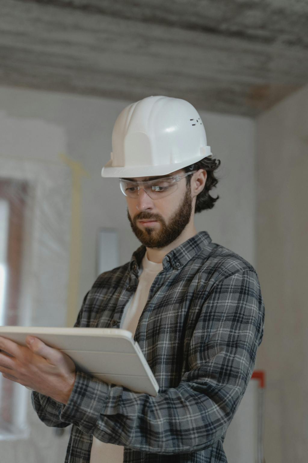 A general contractor stands in the middle of a jobsite with clipboard in hand.
