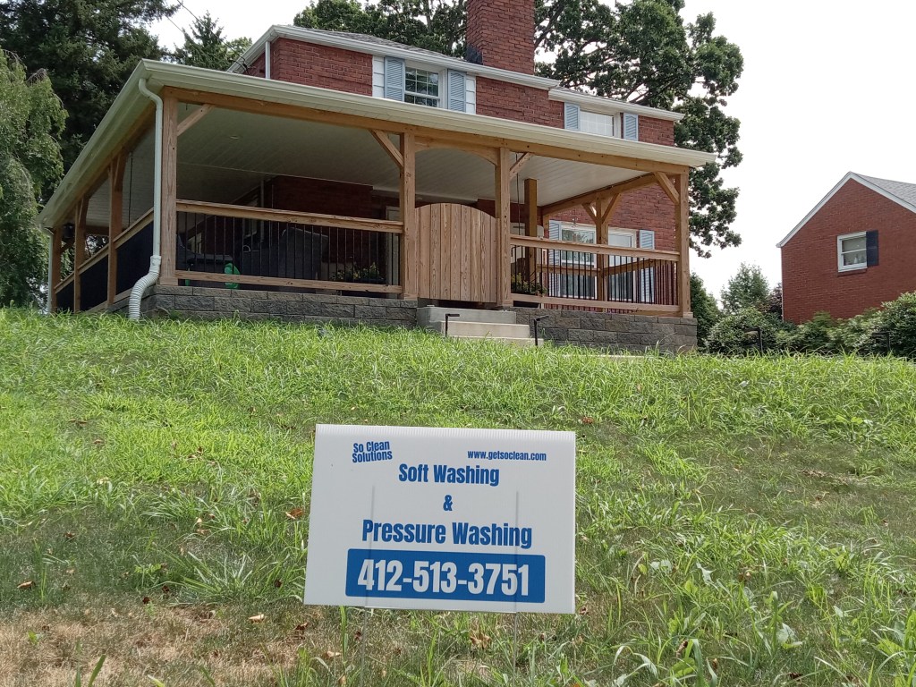 A brick home with a wrap-around porch. Window cleaning and gutter cleaning services have been performed. A So Clean Solutions yard sign is in the foreground.