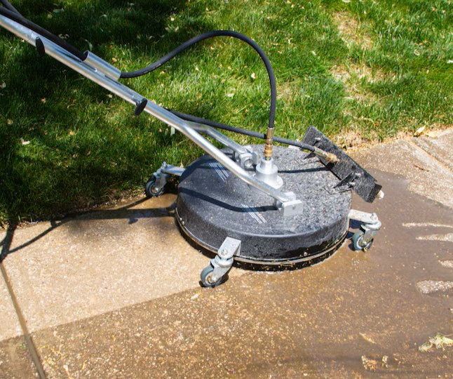 A So Clean Solutions technician uses a surface cleaner to pressure wash a concrete sidewalk.