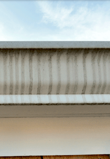 A white aluminum gutter with dark streaks known as tiger striping.