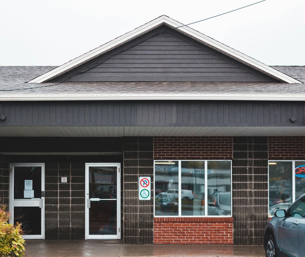 A commercial storefront with clean shingles, clean siding, clean windows and glass doors, and a clean sidewalk.