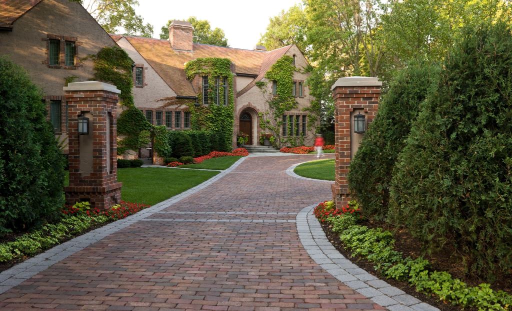 A view of a manor house with a decorative brick driveway, brick and stone columns, and extensive stone and paver block edging.