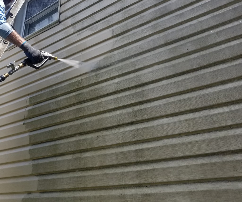 A technician from So Clean Solutions uses a pressure washer to rinse mold, mildew, and algae from vinyl siding on a Pittsburgh area home.