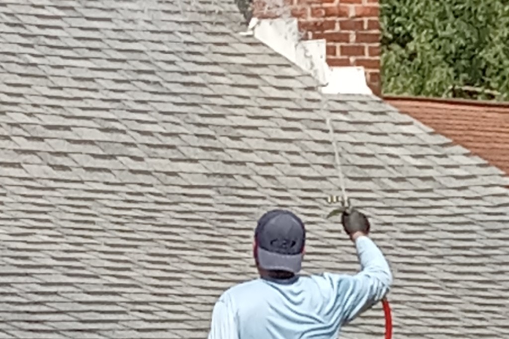 An exterior cleaning technician from So Clean Solutions performs a soft wash cleaning on a shingle roof in Pittsburgh, PA.